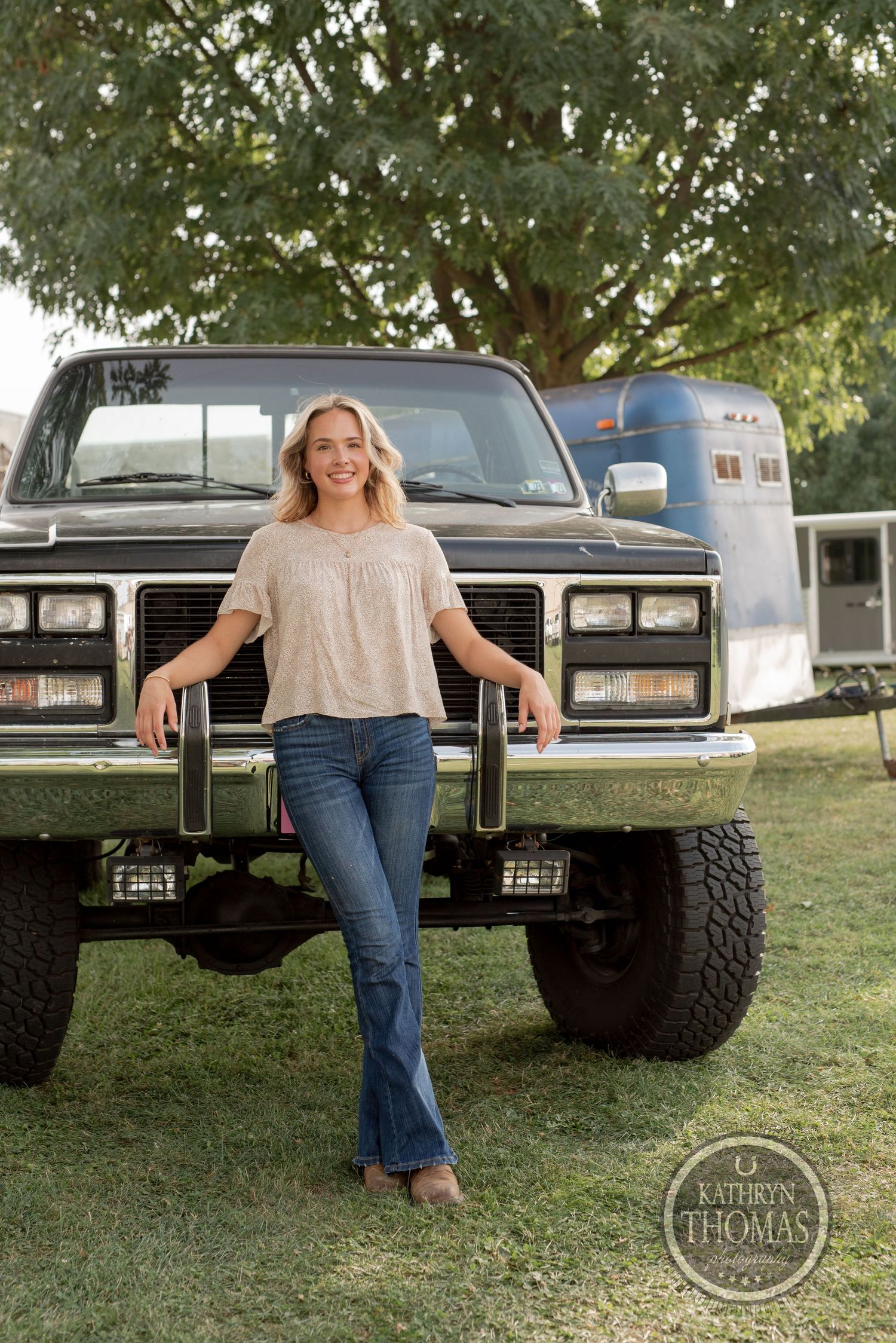 Someone poses in front of a lifted vintage GMC truck and horse trailer.