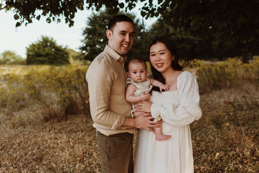 An intimate family portrait outdoors with a baby in a natural setting during golden hour.