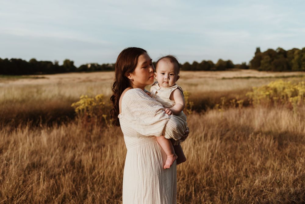 A touching outdoor portrait of a parent and baby against a golden field at sunset.