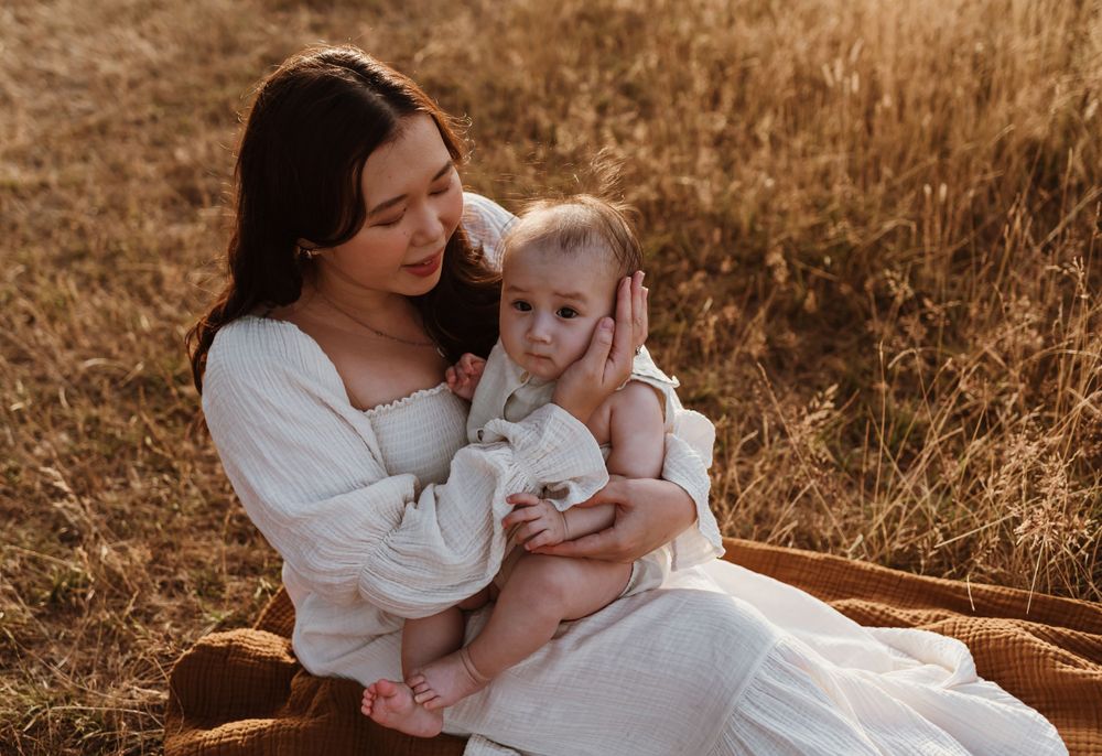 A gentle moment between parent and baby sitting on a blanket in a sun-drenched field.