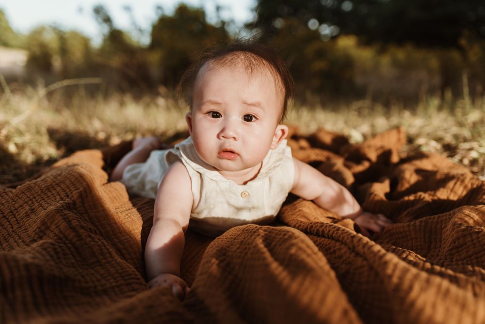 Baby lying on brown blanket outdoors in warm sunlight.