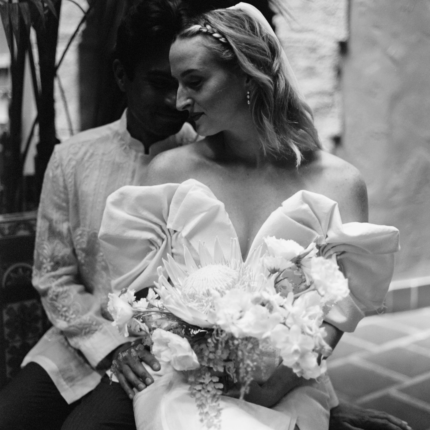 Black and white wedding photo featuring dramatic off-shoulder dress with bow details and floral bouquet.