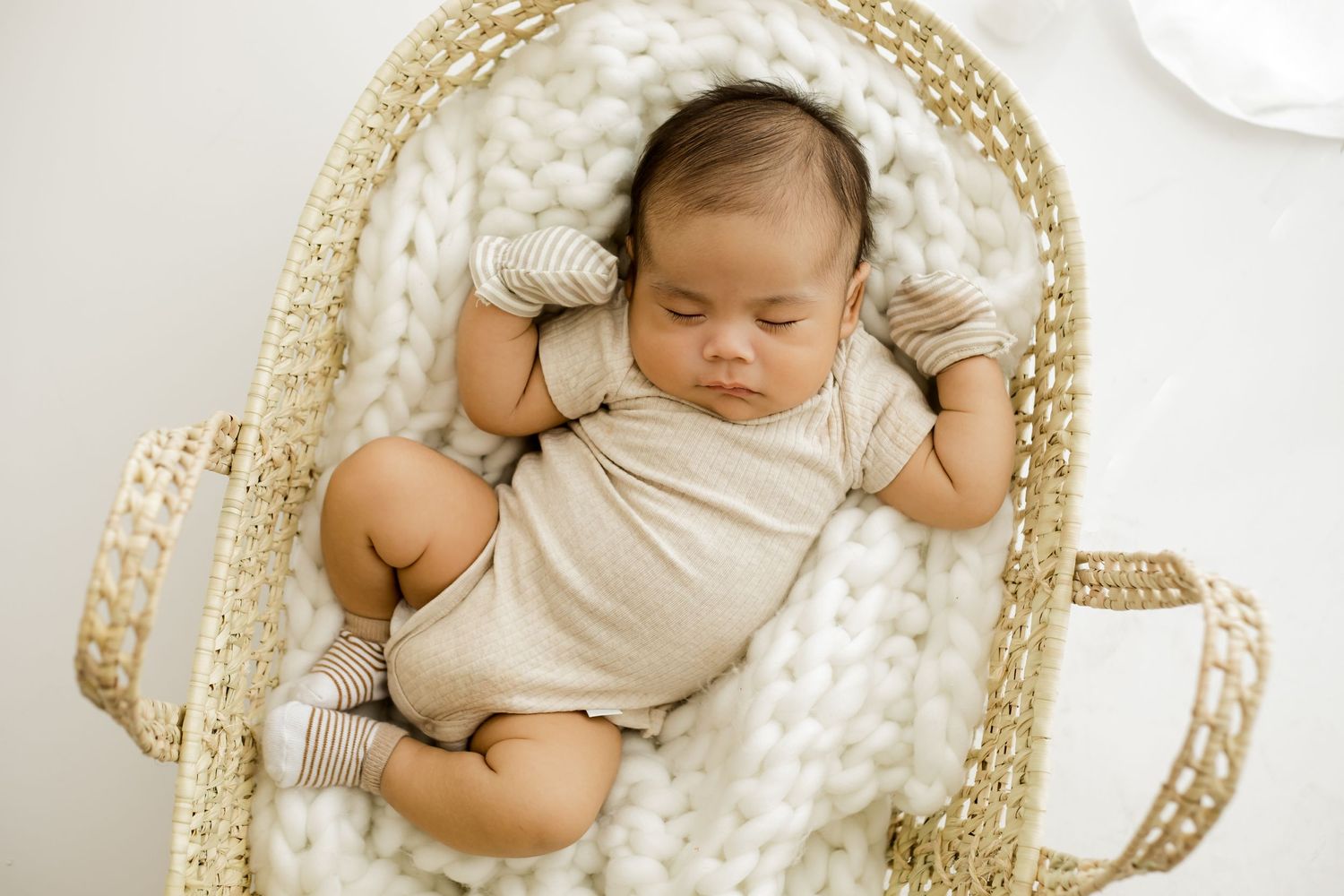 Natural posed baby boy in a bassinette in the lifestyle room of the white studio for his newborn lifestyle session.