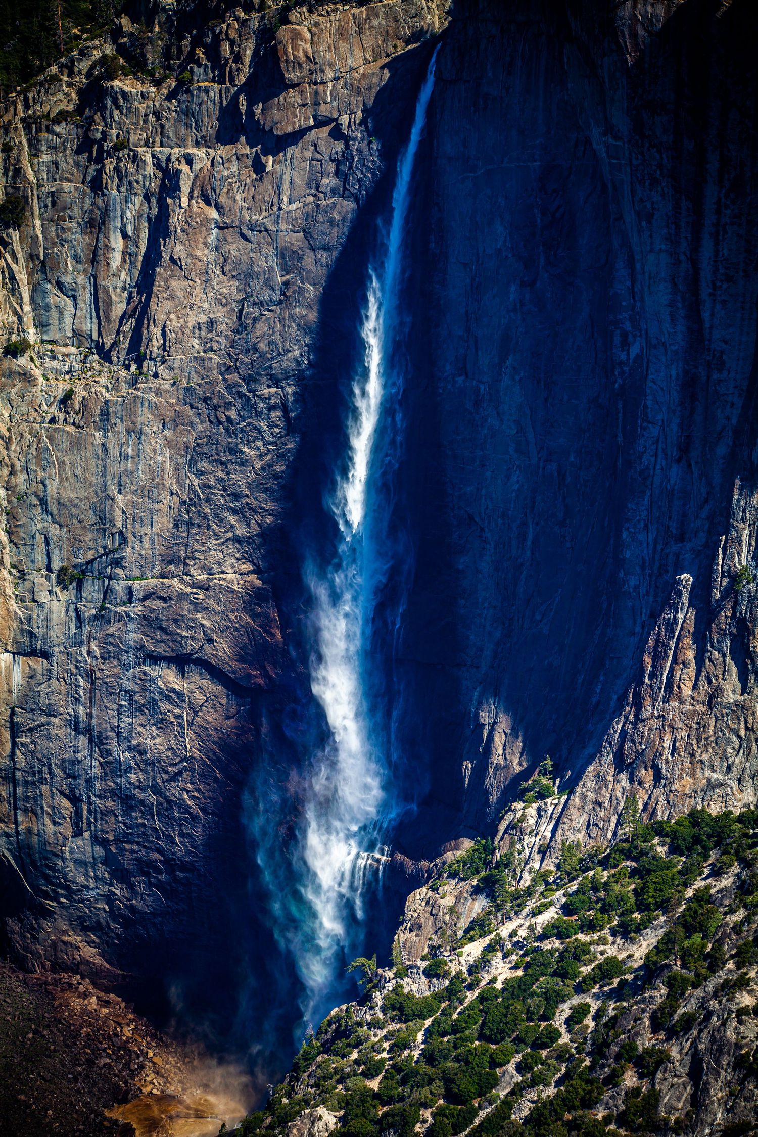 Dramatic waterfall cascading down steep granite cliffs amidst rugged mountain terrain.