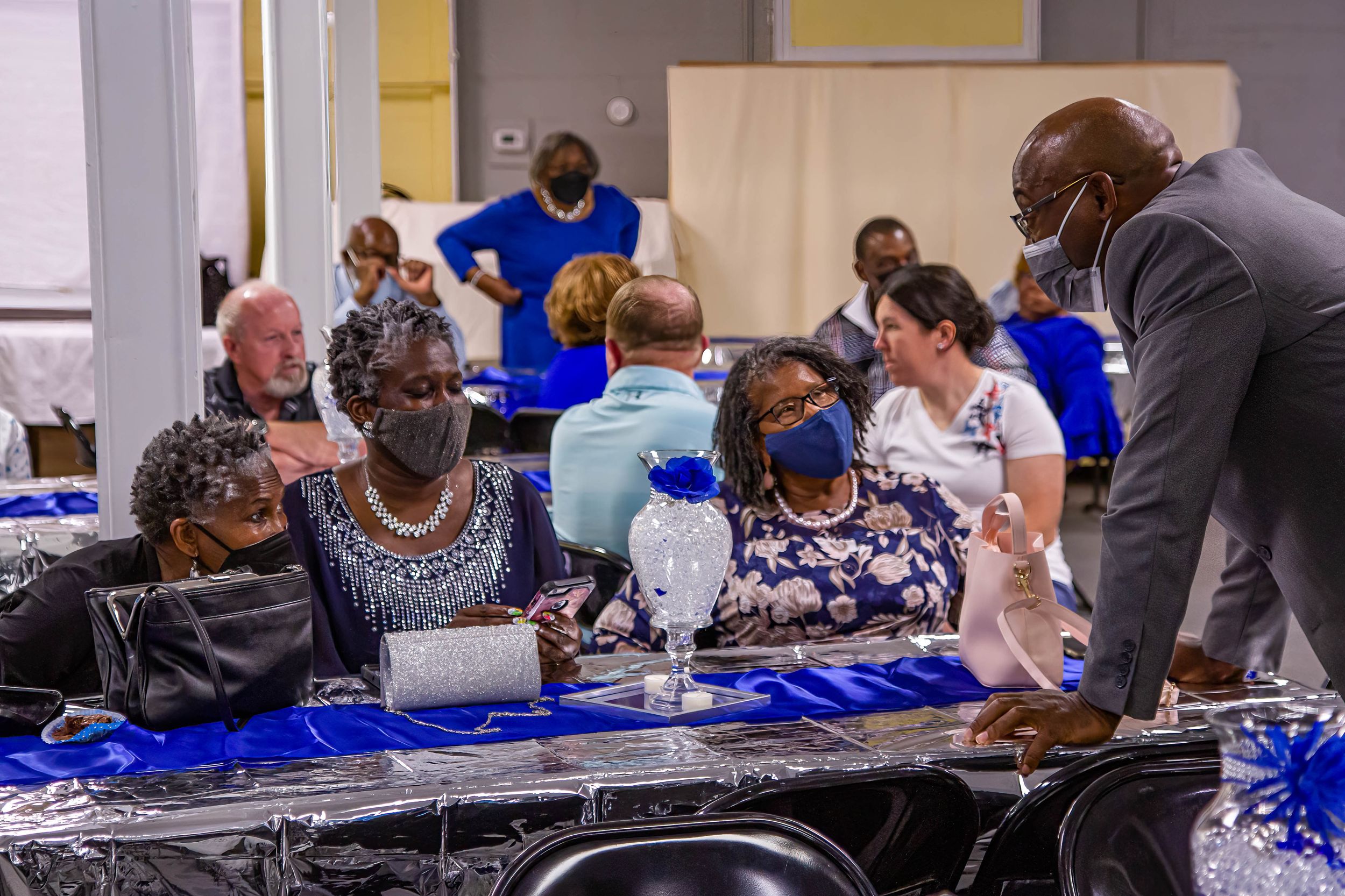Group gathered around tables with blue tablecloths at a community event.
