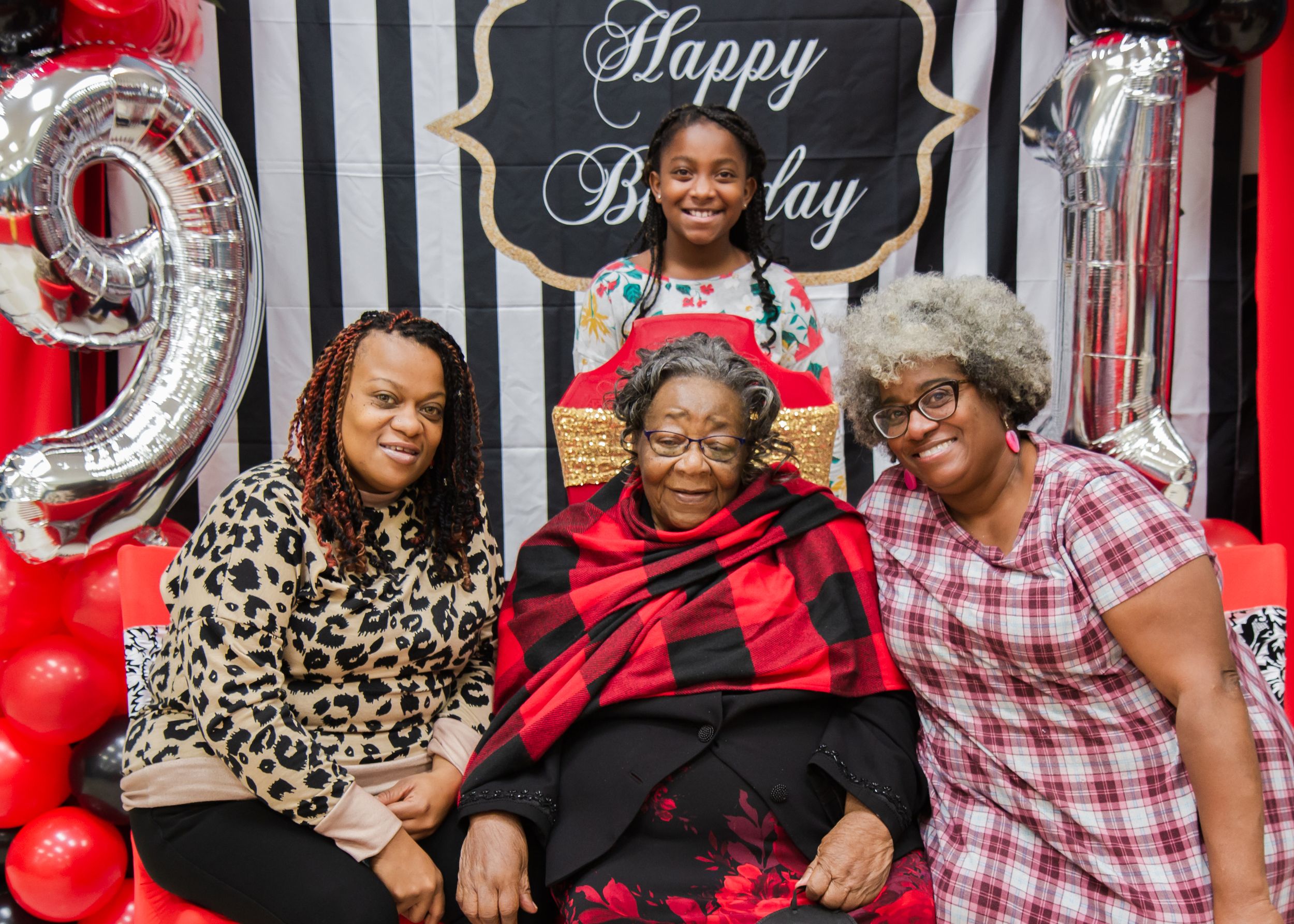 Family gathering at birthday celebration with black and white backdrop and red balloons.