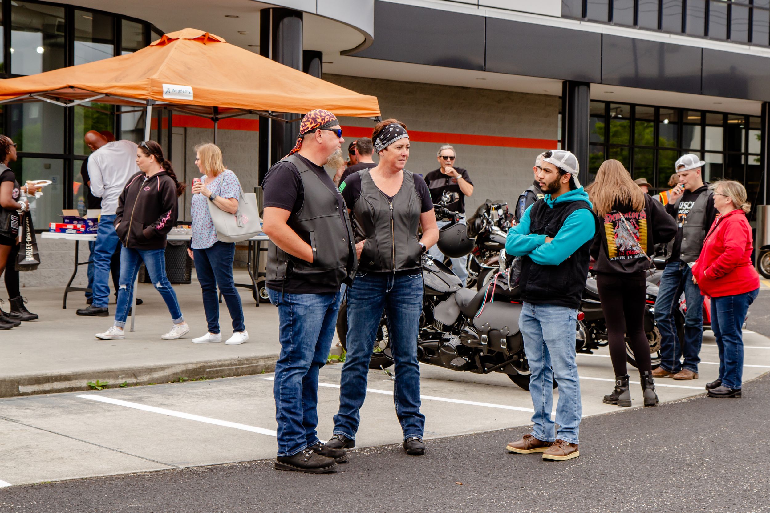 People gather outside under orange umbrellas at a casual outdoor event.