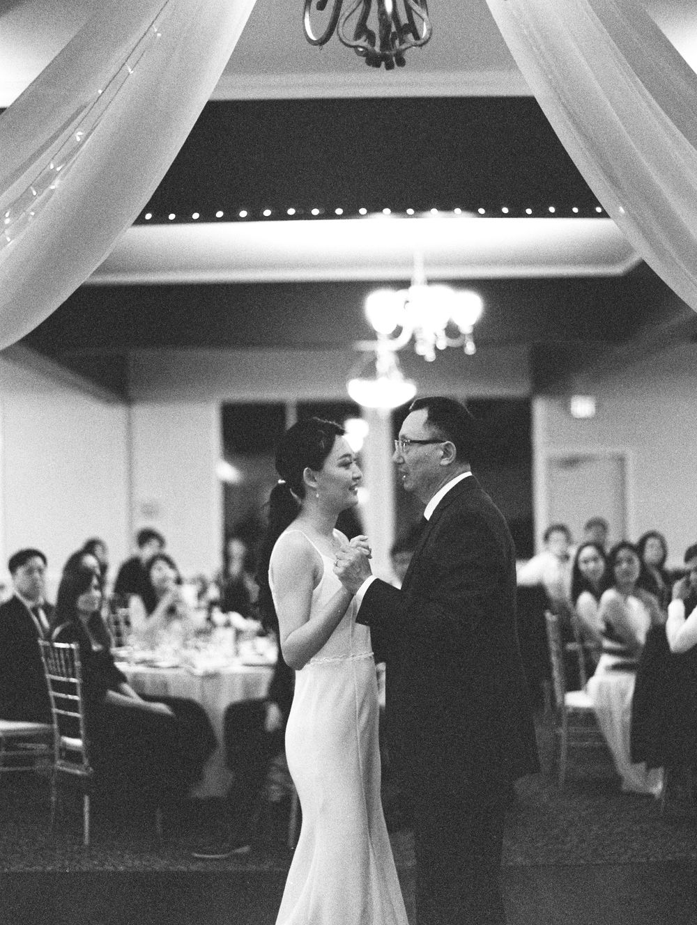 A couple shares their first dance at a wedding reception beneath elegant string lights and draped fabric.