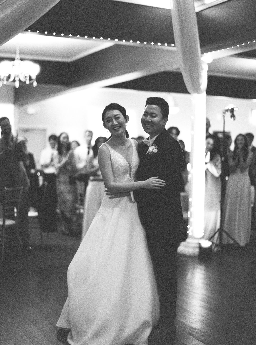 Couple dances together in wedding attire under draped fabric and chandeliers.