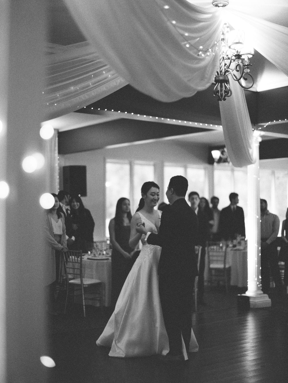 Elegant wedding reception scene with couple dancing under draped fabric and twinkling lights.