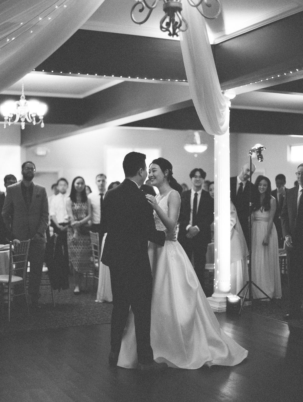 Wedding reception first dance moment captured in black and white under elegant chandelier lighting.