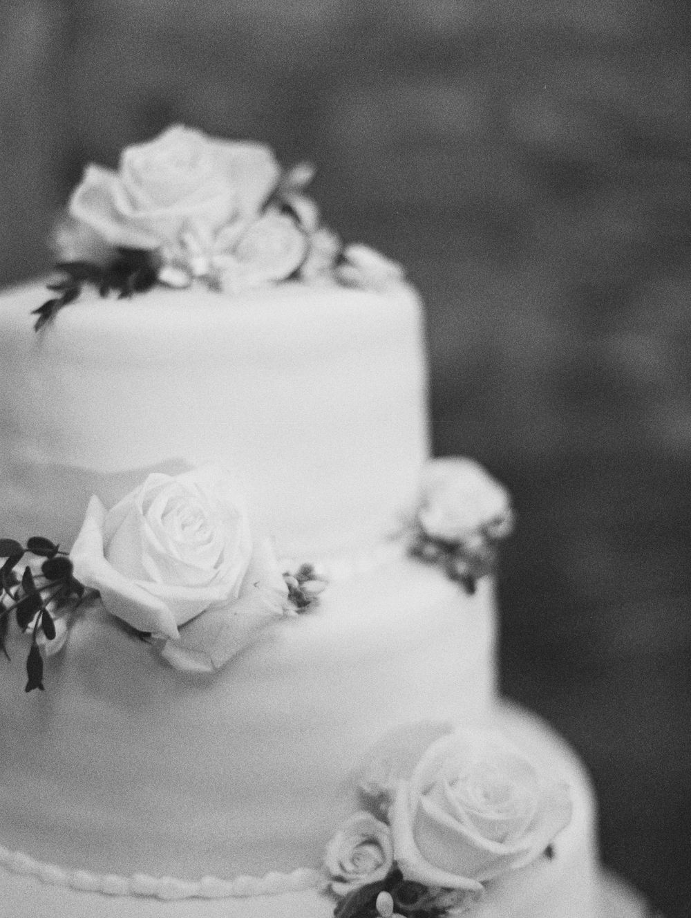 Elegant white tiered wedding cake decorated with delicate roses in black and white photography.