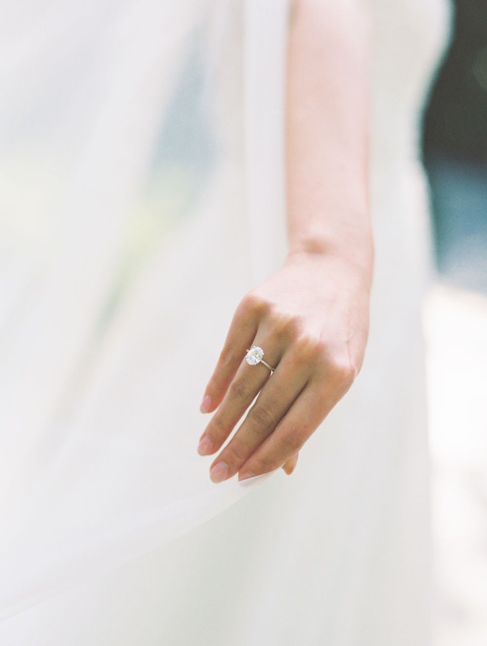 A delicate hand wearing a diamond engagement ring against a soft white background.