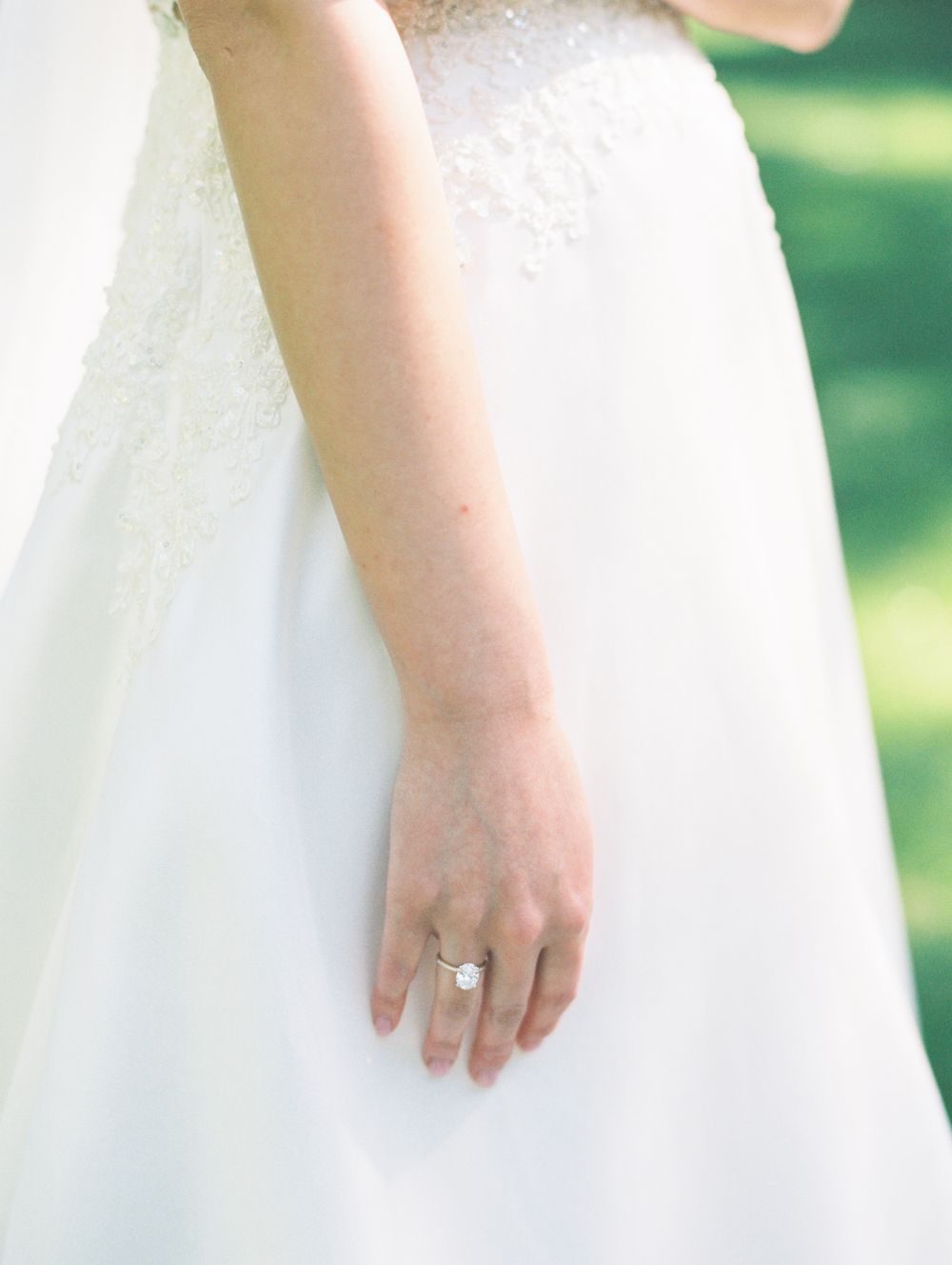 A bride's hand wearing an engagement ring against the backdrop of her white wedding dress.