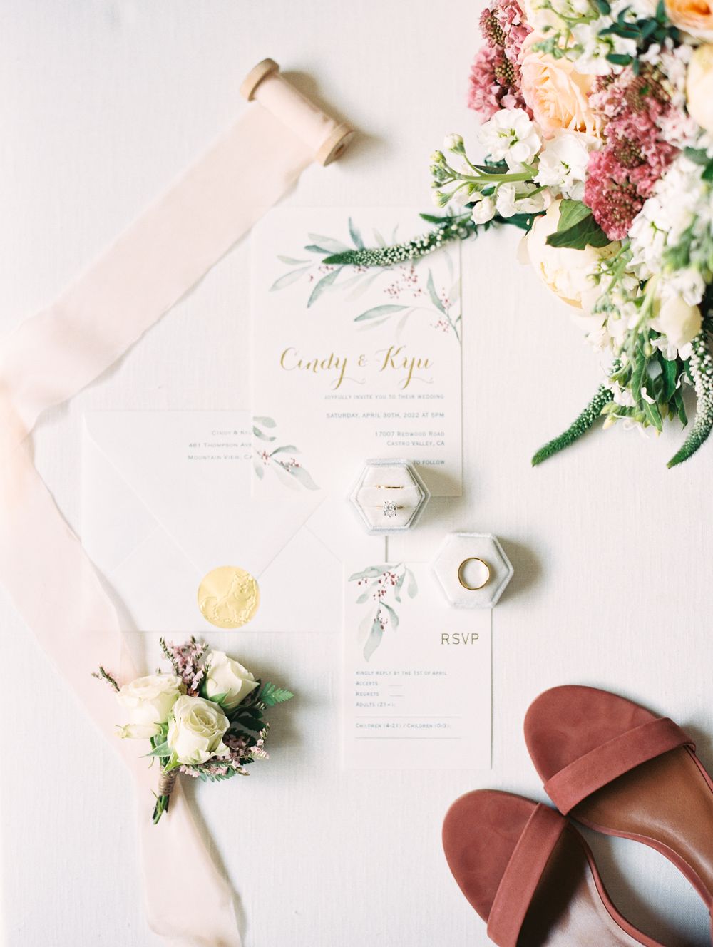 Wedding details flatlay with invitation, ring boxes, brown shoes and fresh flowers.