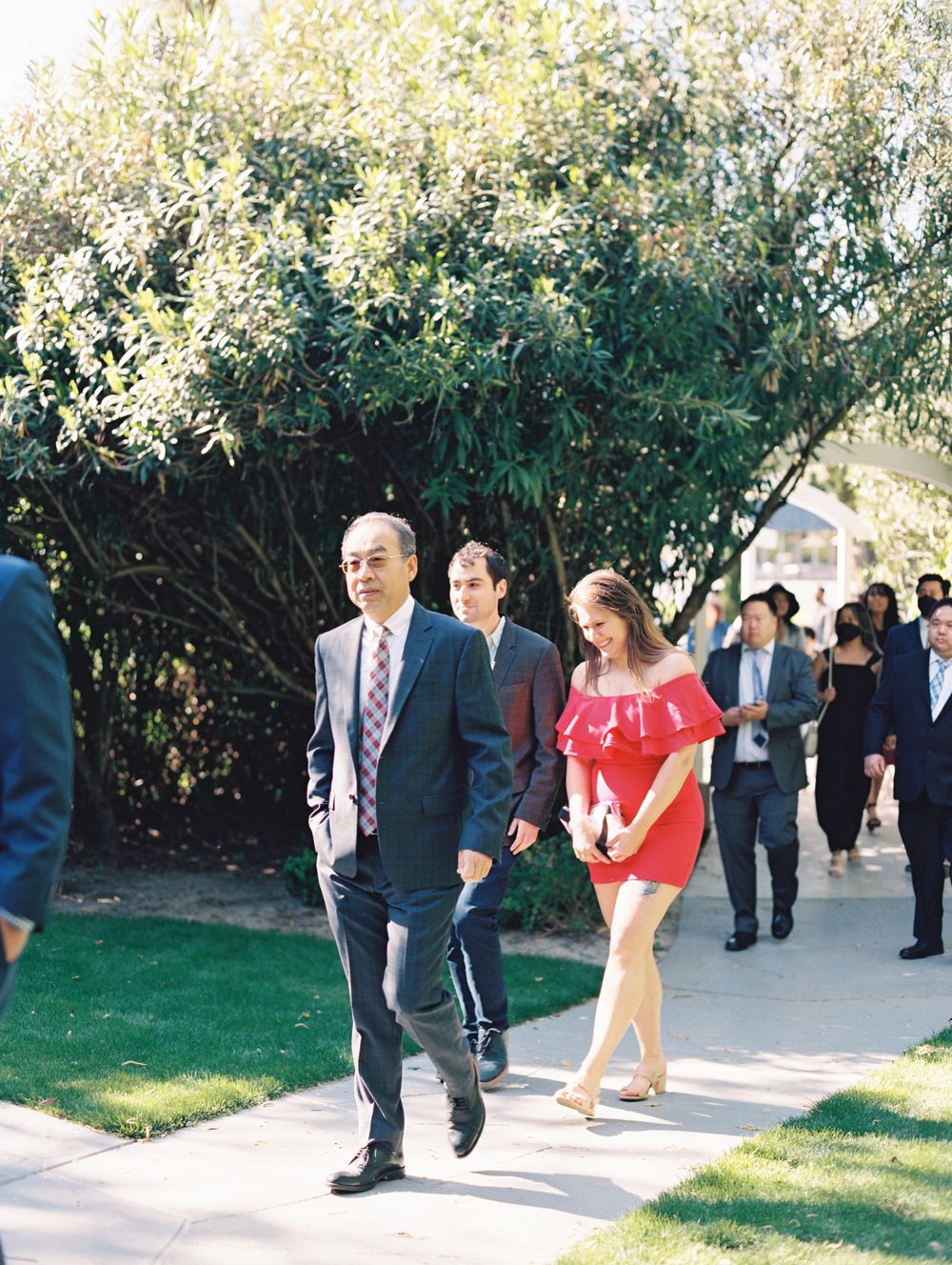 Wedding guests walking along a garden path lined with lush greenery.