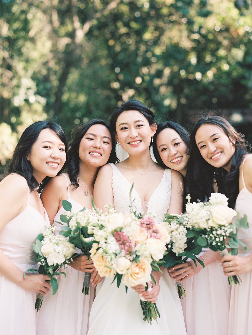 Wedding party with pastel bouquets sharing joyful moment in garden setting.