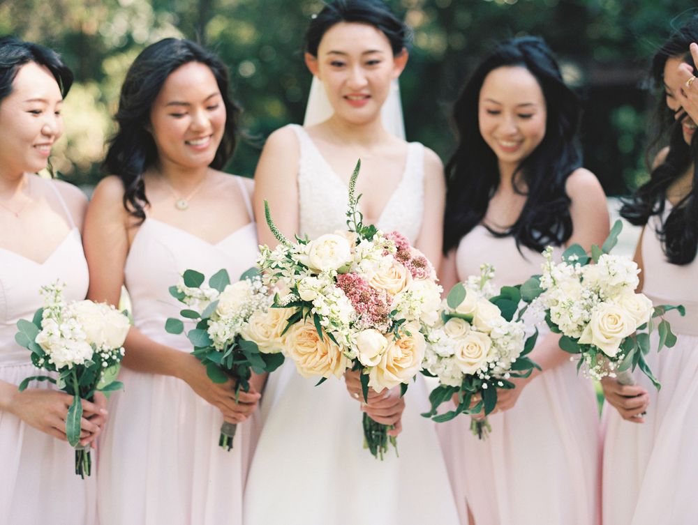 Bridal party displaying elegant bouquets of mixed flowers in soft pastel colors.