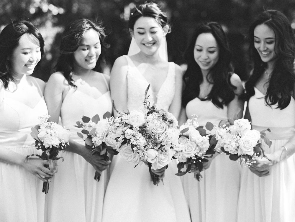 Black and white photo of bridal party with elegant floral bouquets in garden setting.