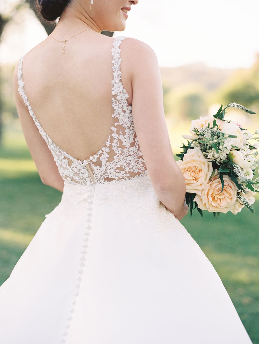 Back view of wedding dress showing intricate lace detail and buttons in soft natural light.