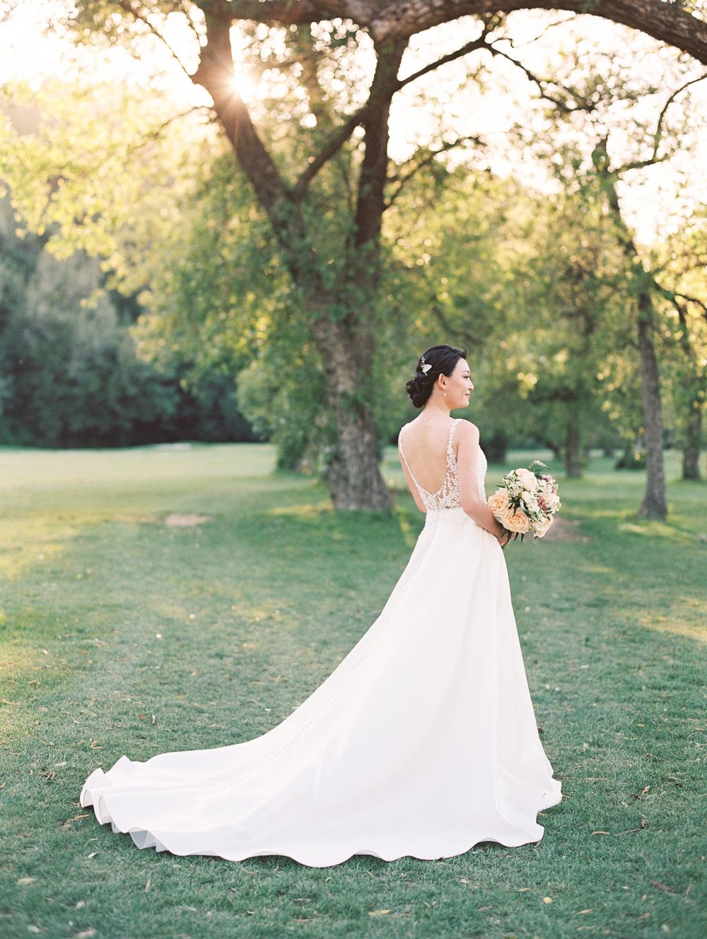 Wedding dress with flowing train photographed in sunlit garden setting.