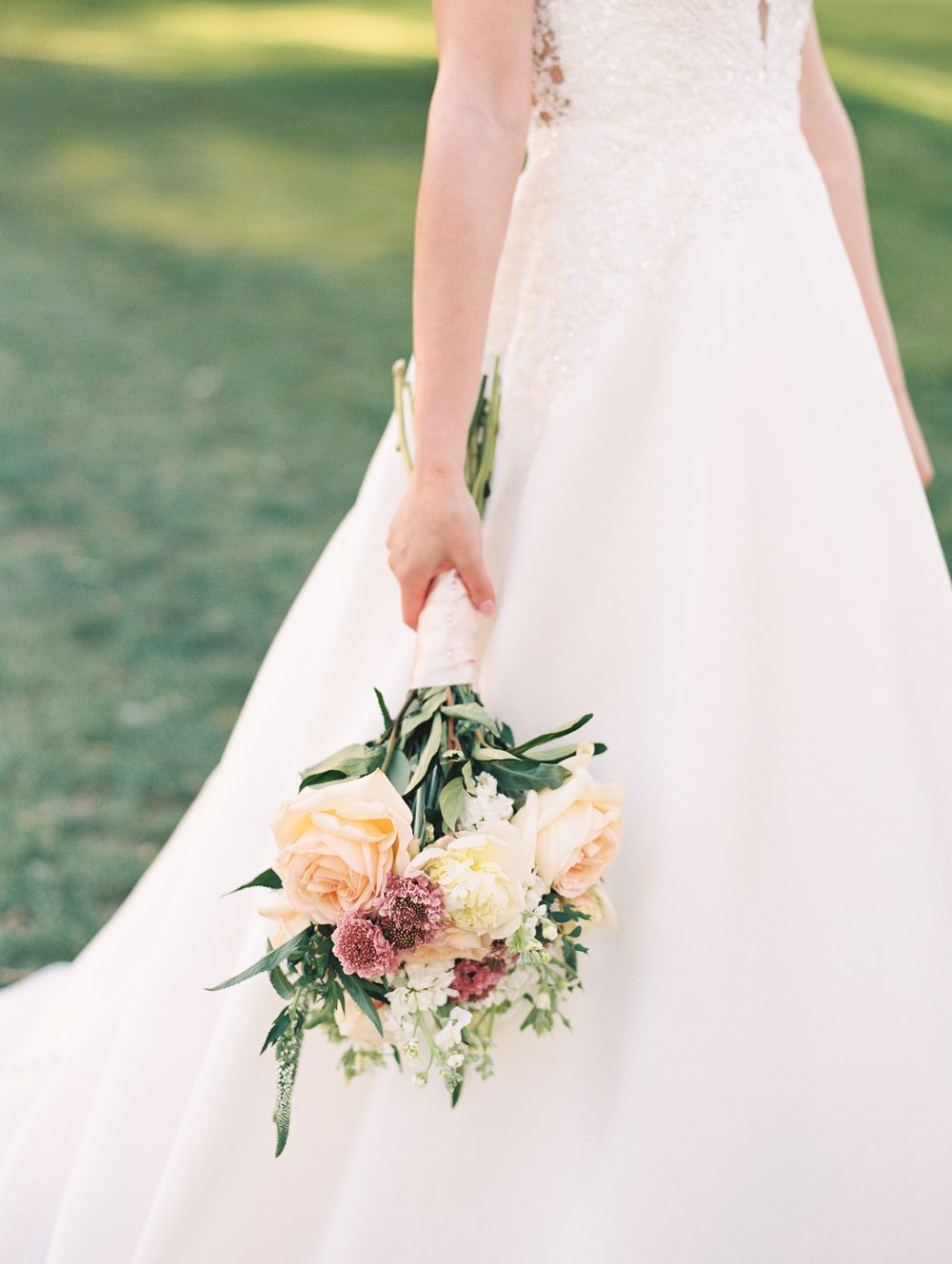 Bride holding a romantic bouquet with peach roses and greenery against white wedding dress.