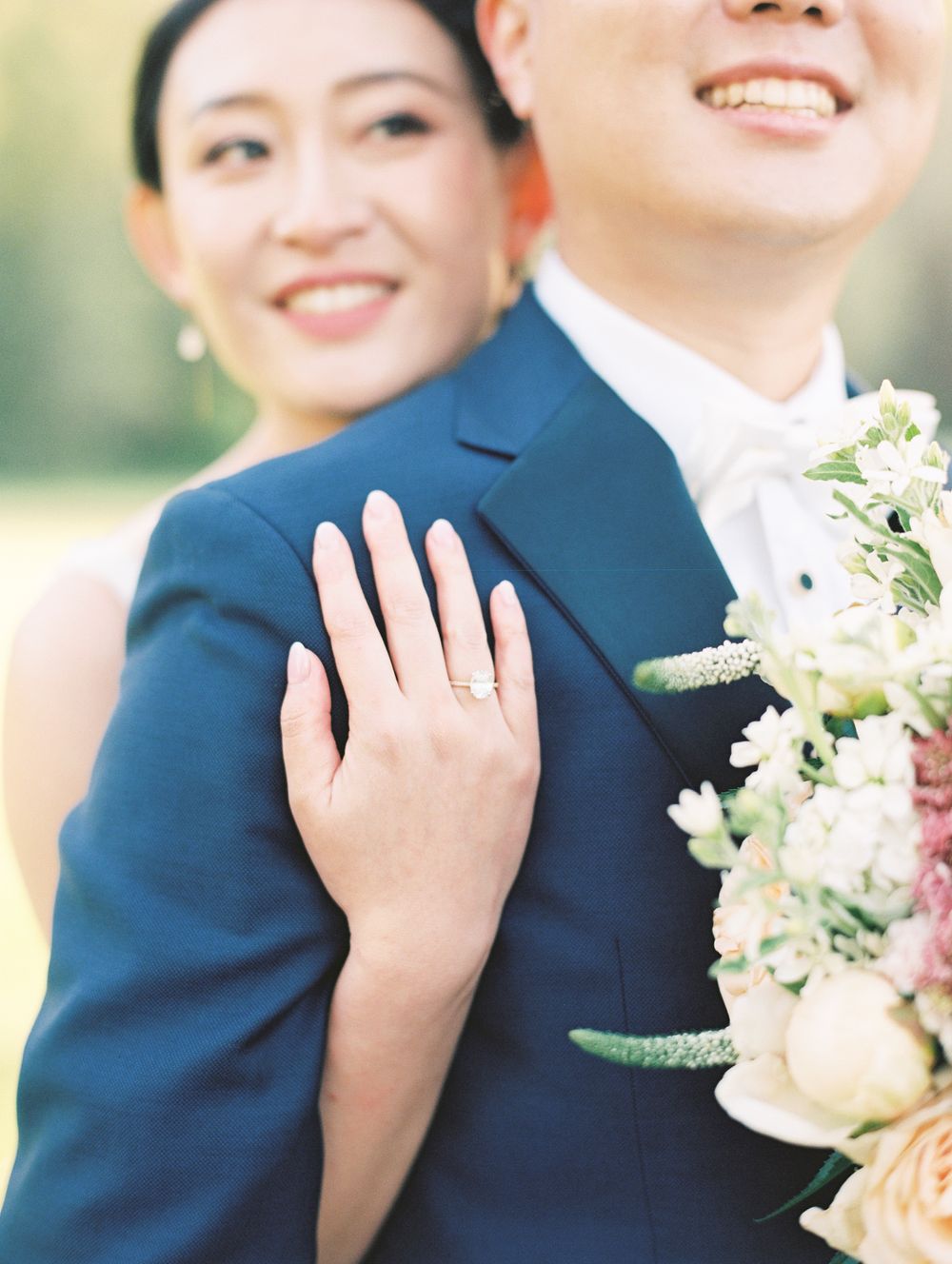 Wedding couple detail shot showing ring and floral boutonniere against navy suit.
