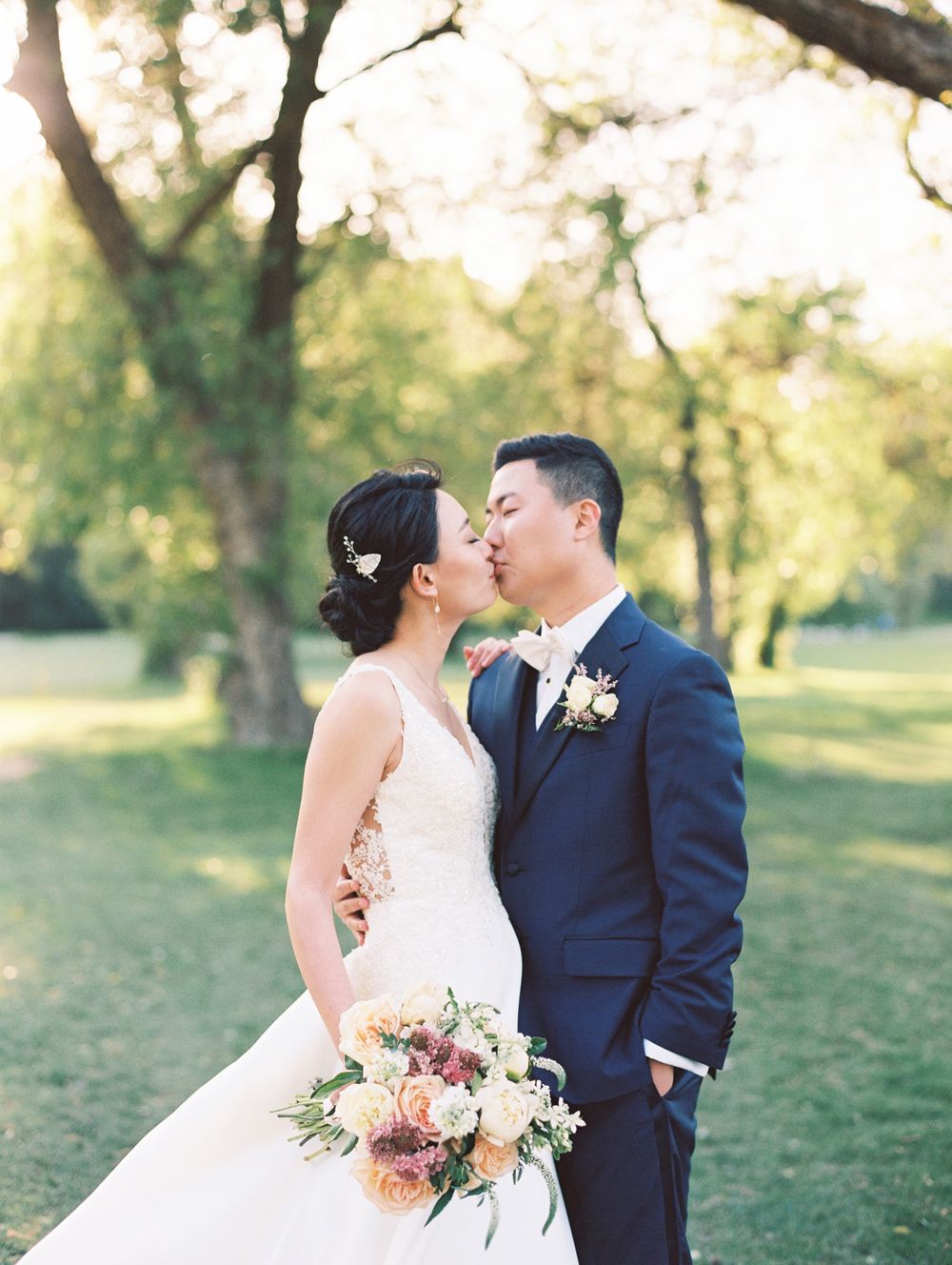 Romantic wedding portrait with soft sunlight filtering through trees.
