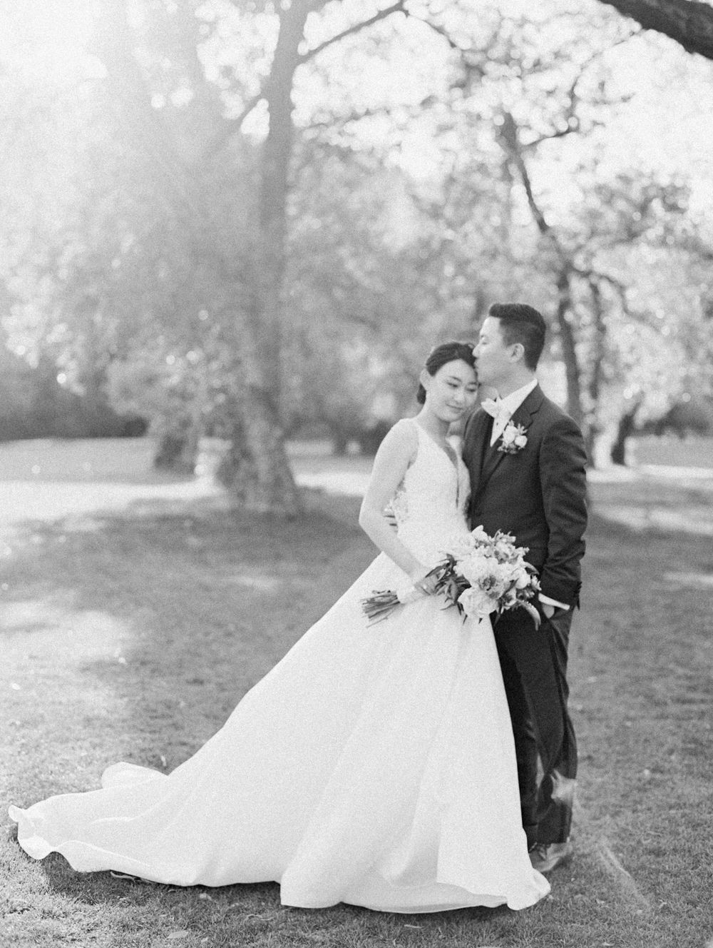 Black and white wedding portrait in a park setting with dramatic light.