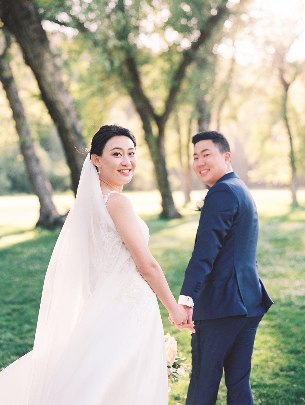 Wedding couple holding hands in a sun-drenched garden setting.