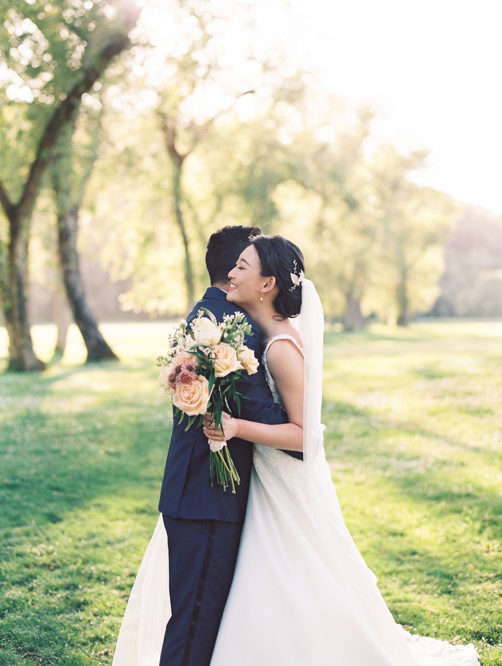 A newlywed couple embraces in a romantic outdoor setting with peach and white roses.