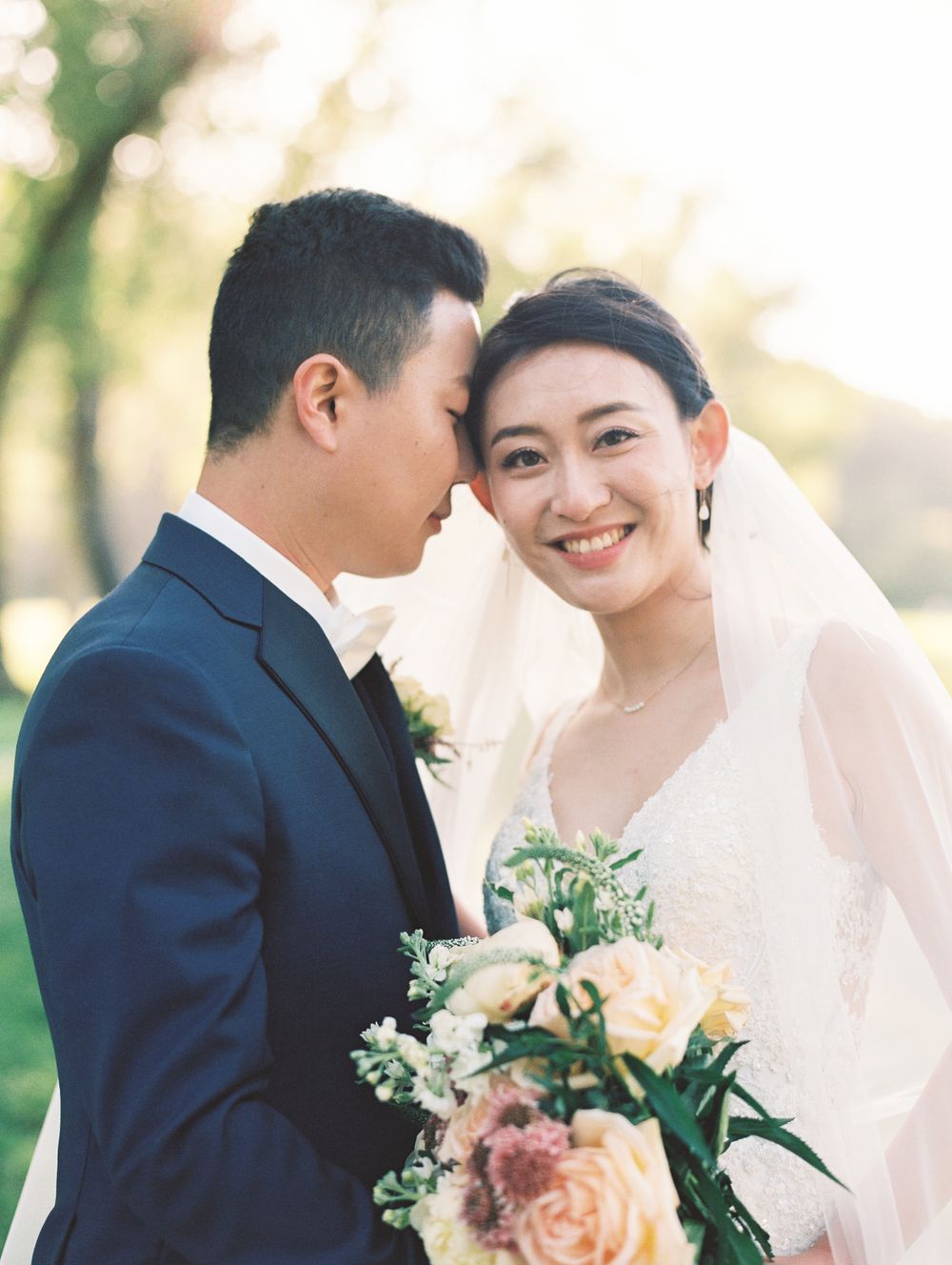A wedding couple shares an intimate moment outdoors while holding a floral bouquet.