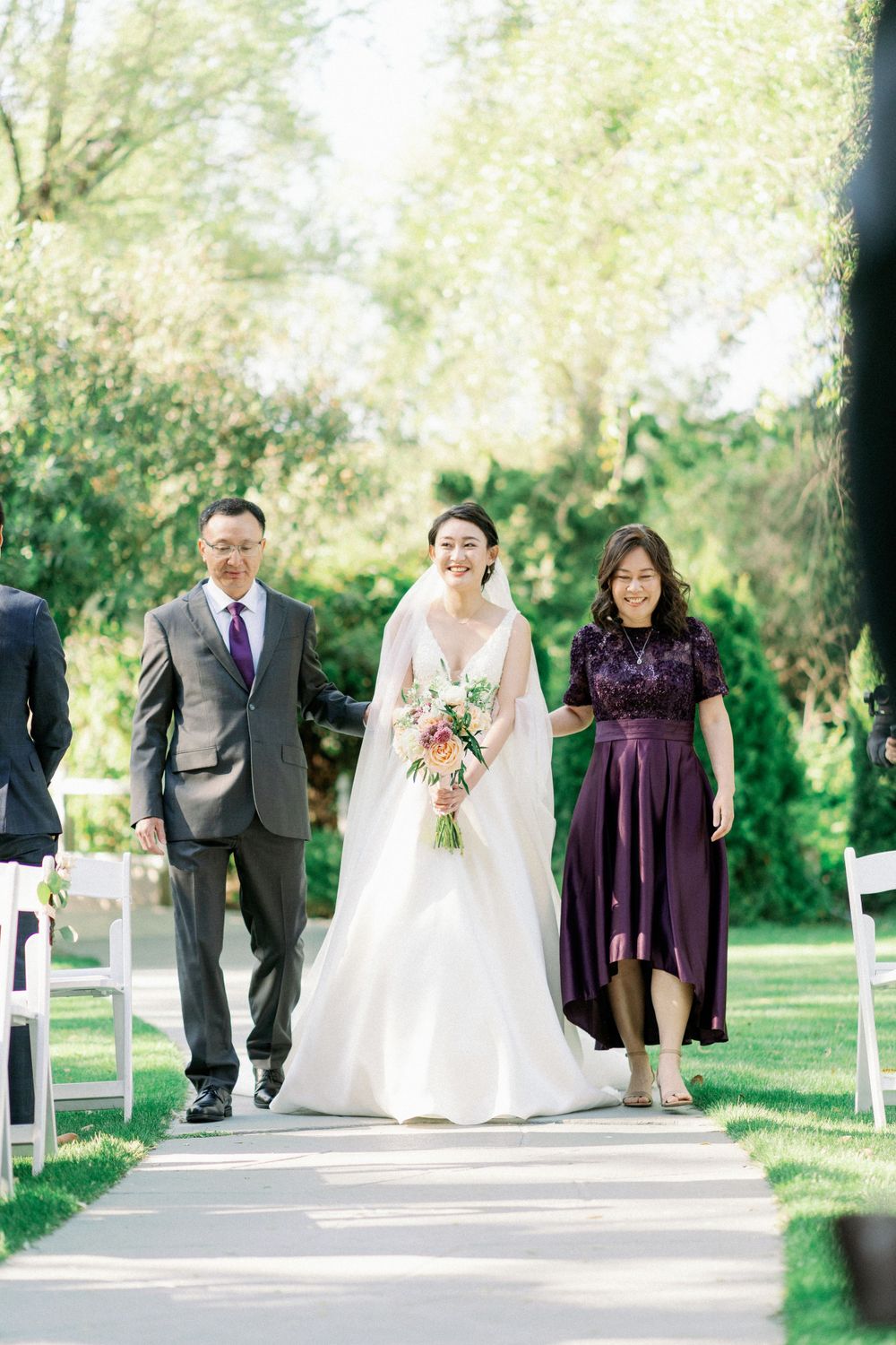 Wedding party walking down outdoor ceremony path with bride in white gown holding pink bouquet.