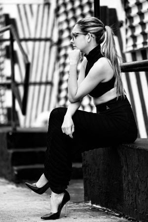 Black and white photo of person in black dress sitting on bench with dramatic shadows.