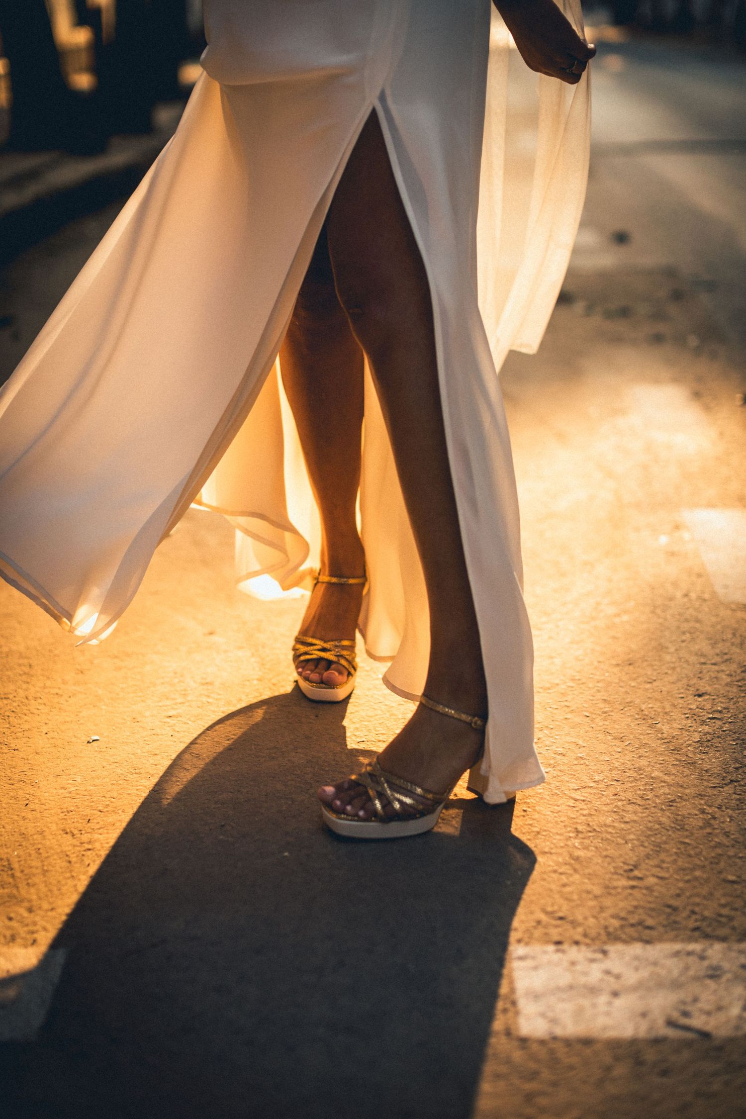 Artistic photo of wedding couple's feet and flowing dress illuminated by golden sunlight.