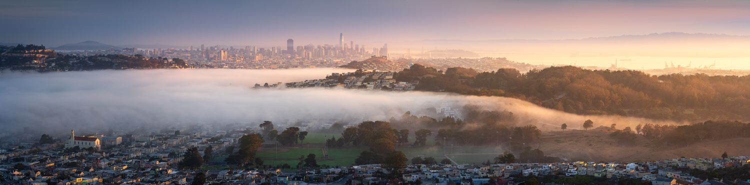 Panoramic cityscape of San Francisco under dramatic sunset sky with fog rolling over Golden Gate Bridge and hills.