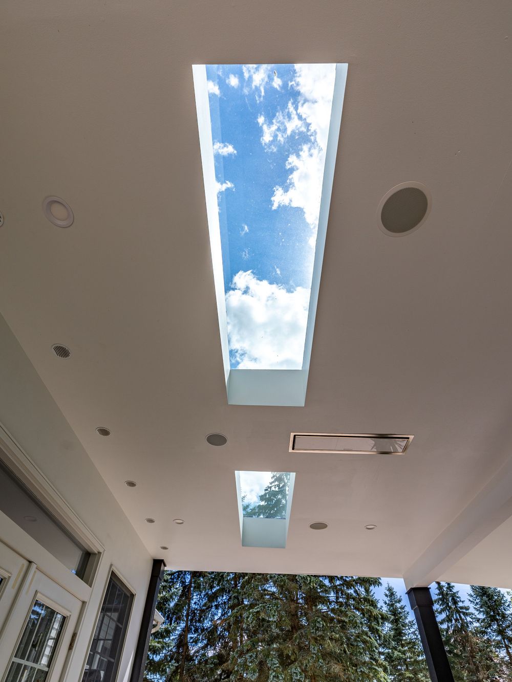 Rectangular skylights in white ceiling revealing blue sky and clouds above.