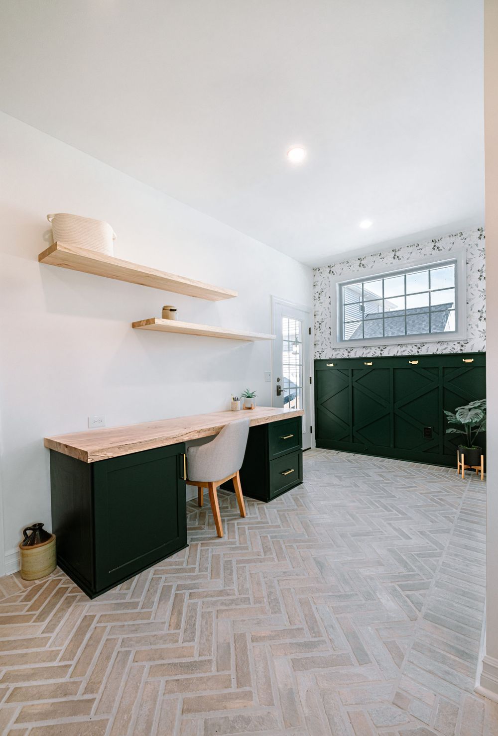 Home office space with dark green cabinets, wooden shelves and herringbone flooring.