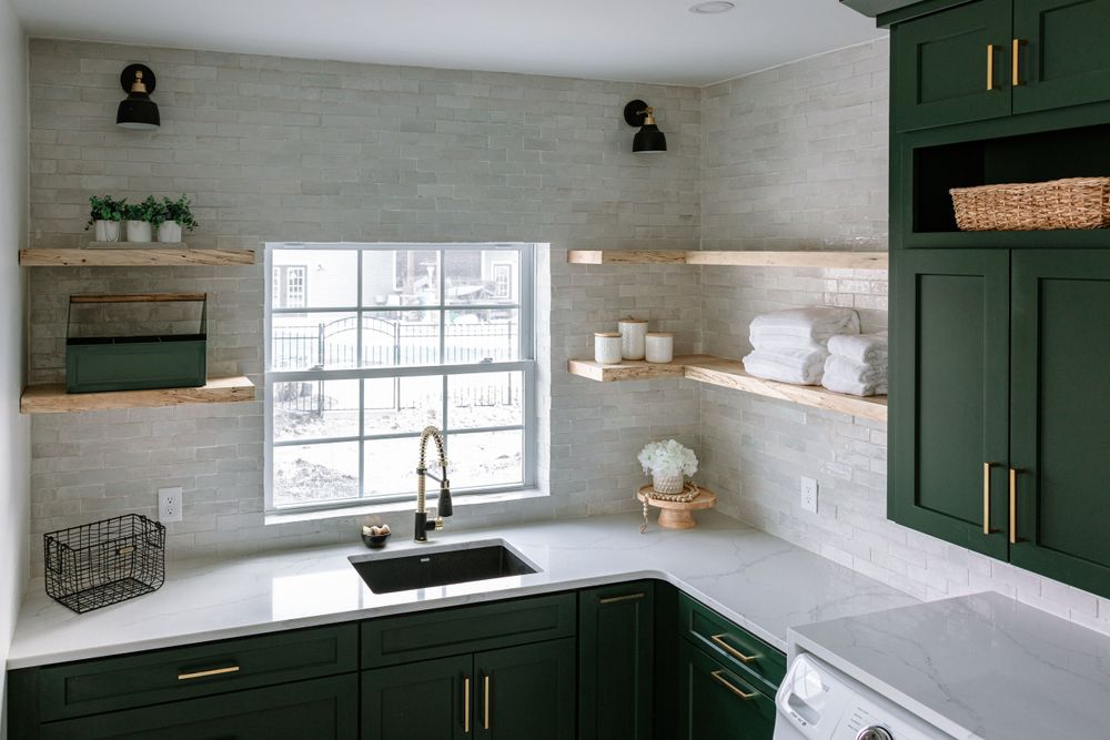 Elegant utility room with green cabinets, floating shelves and white countertops.