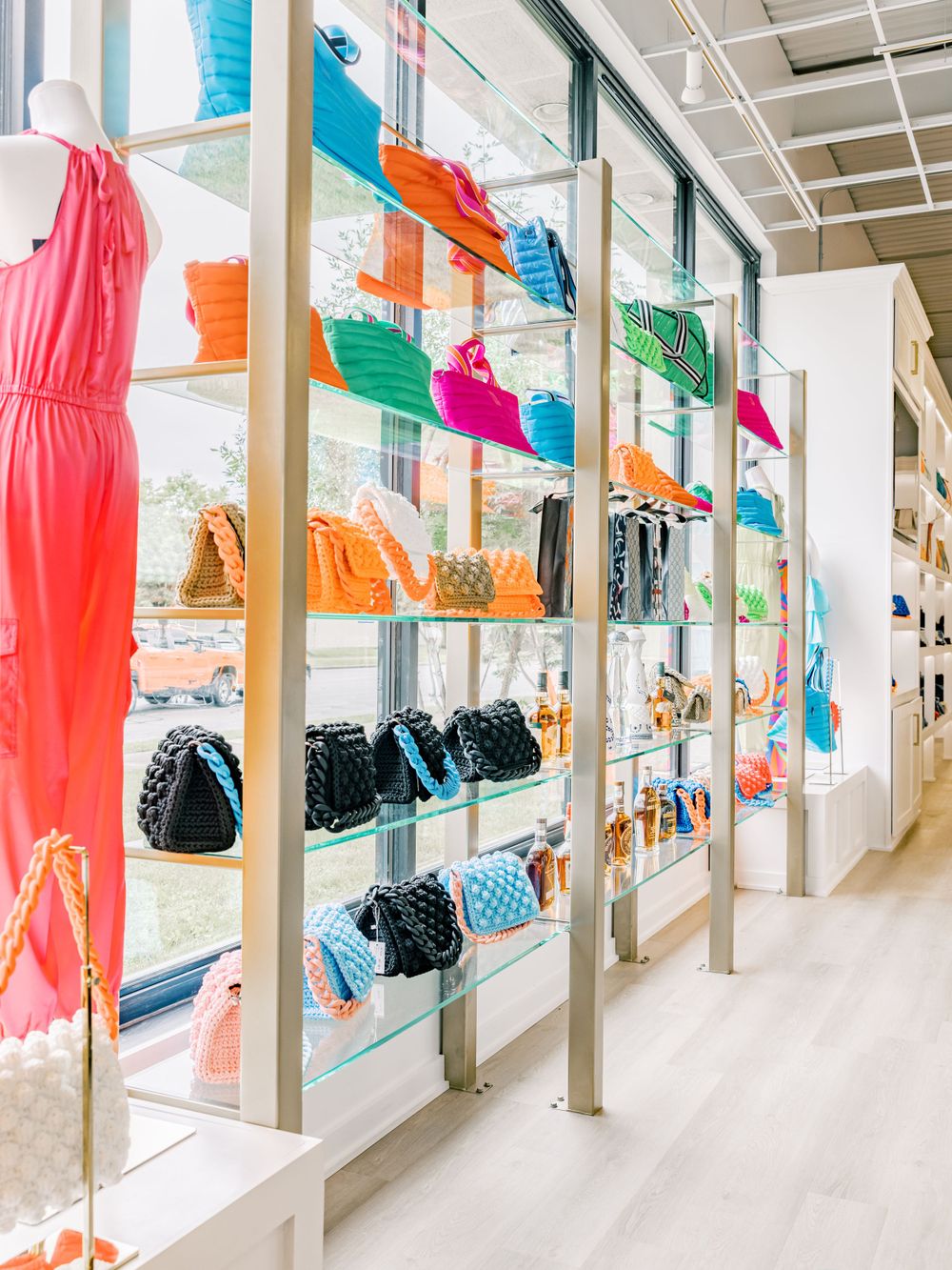 Vibrant display of handbags and accessories in various colors on glass shelving with metal supports.