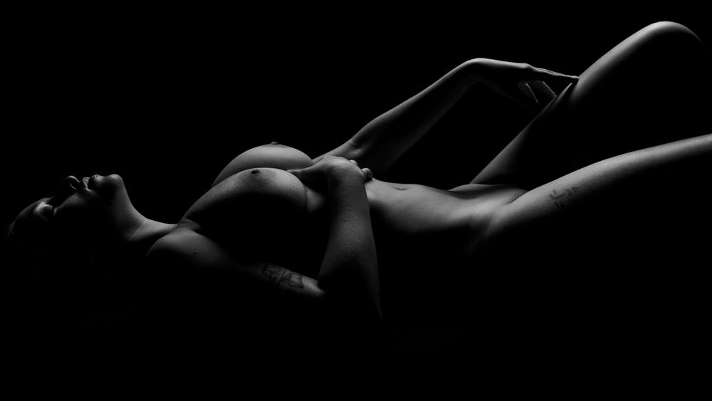 Low key photograph of reclining figure with dramatic shadow play.