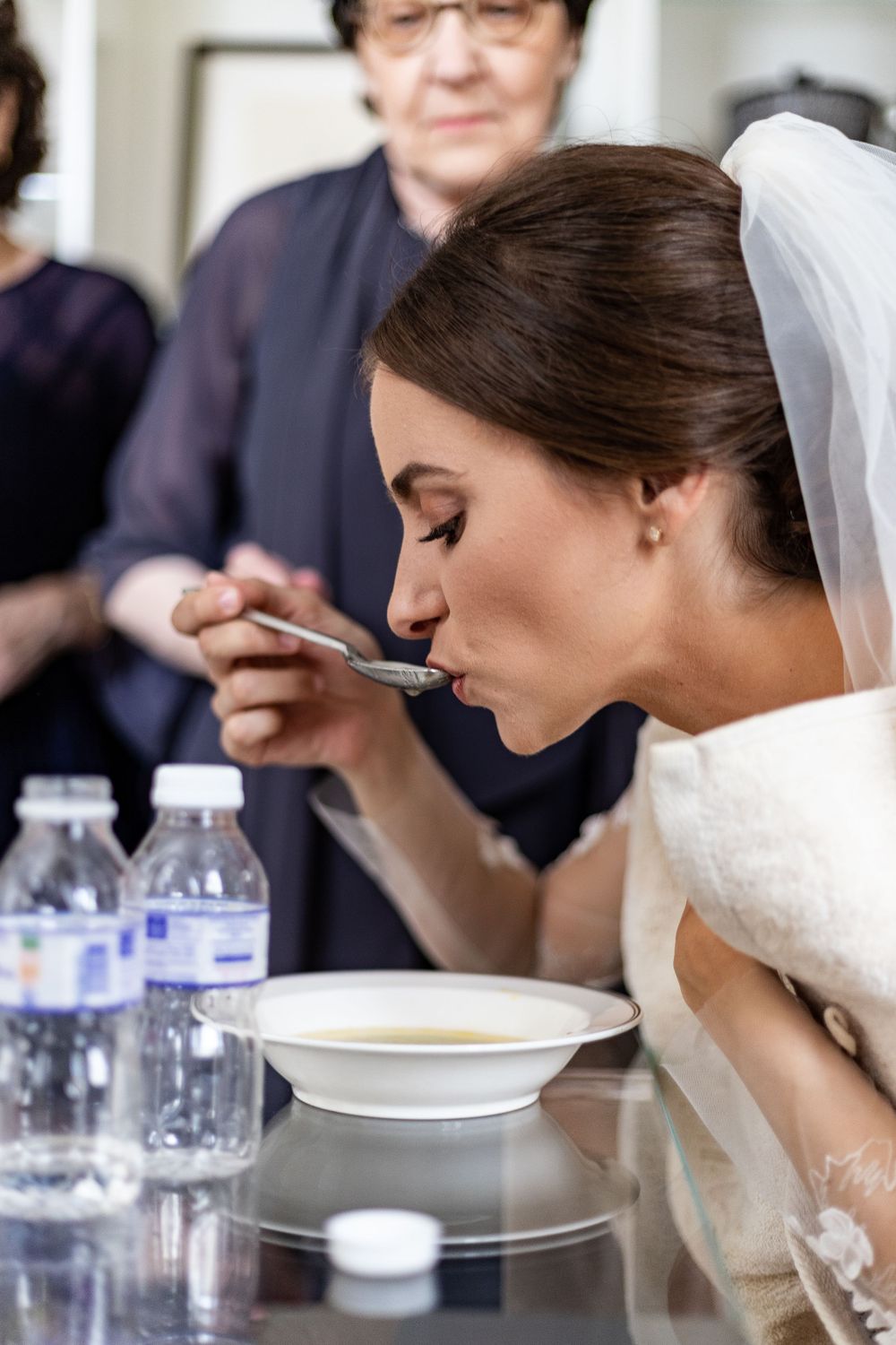 A bride in white dress and veil eats soup from a spoon during her wedding day. traditional ceremony