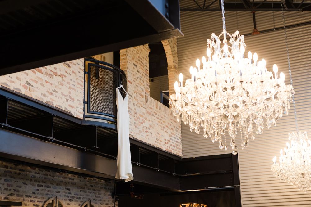 An elegant crystal chandelier hangs from an industrial ceiling with exposed brick walls.