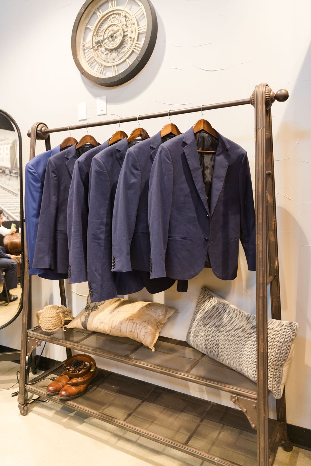 Navy blue suit jackets hanging on an industrial clothing rack with decorative pillows and accessories below.