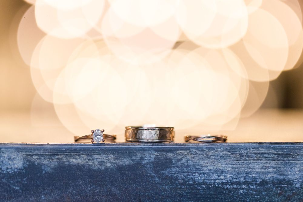 Three wedding rings displayed in a row on a dark surface against a soft bokeh background.
