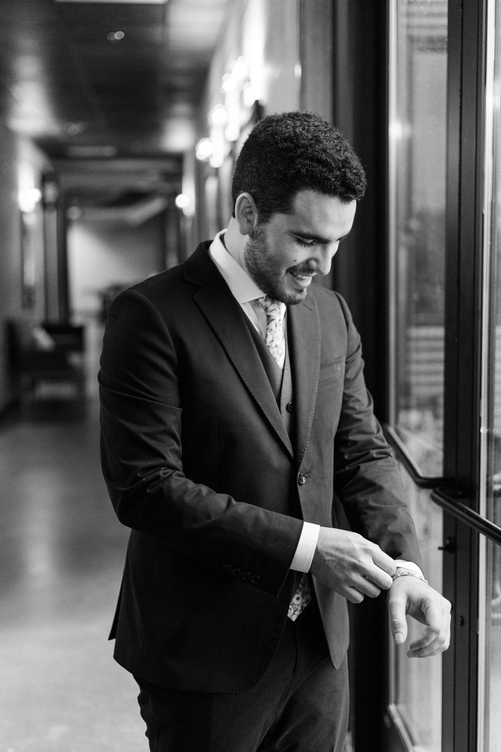 Black and white candid photo of someone in formal attire smiling near a window.