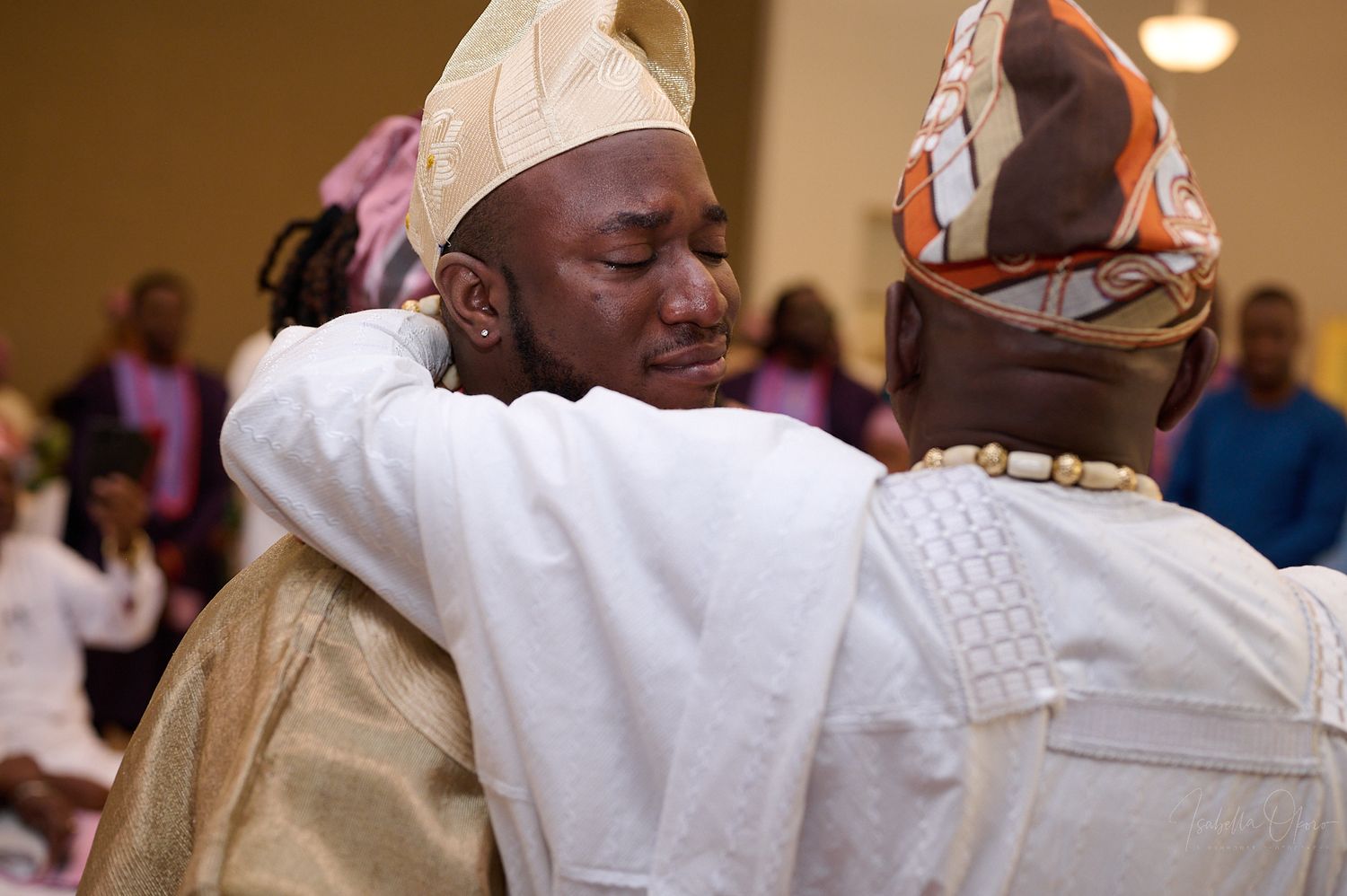 Two people in traditional West African clothing embrace during a celebration event.