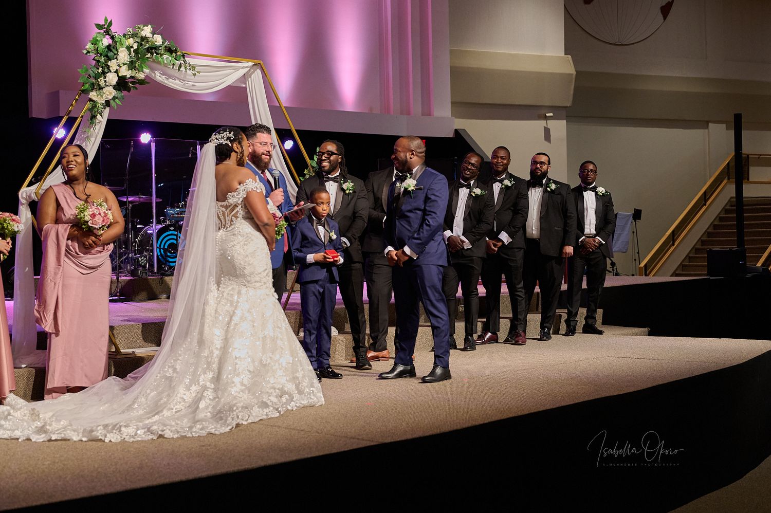 Wedding ceremony under an elegant floral arch with wedding party lined up on stage.