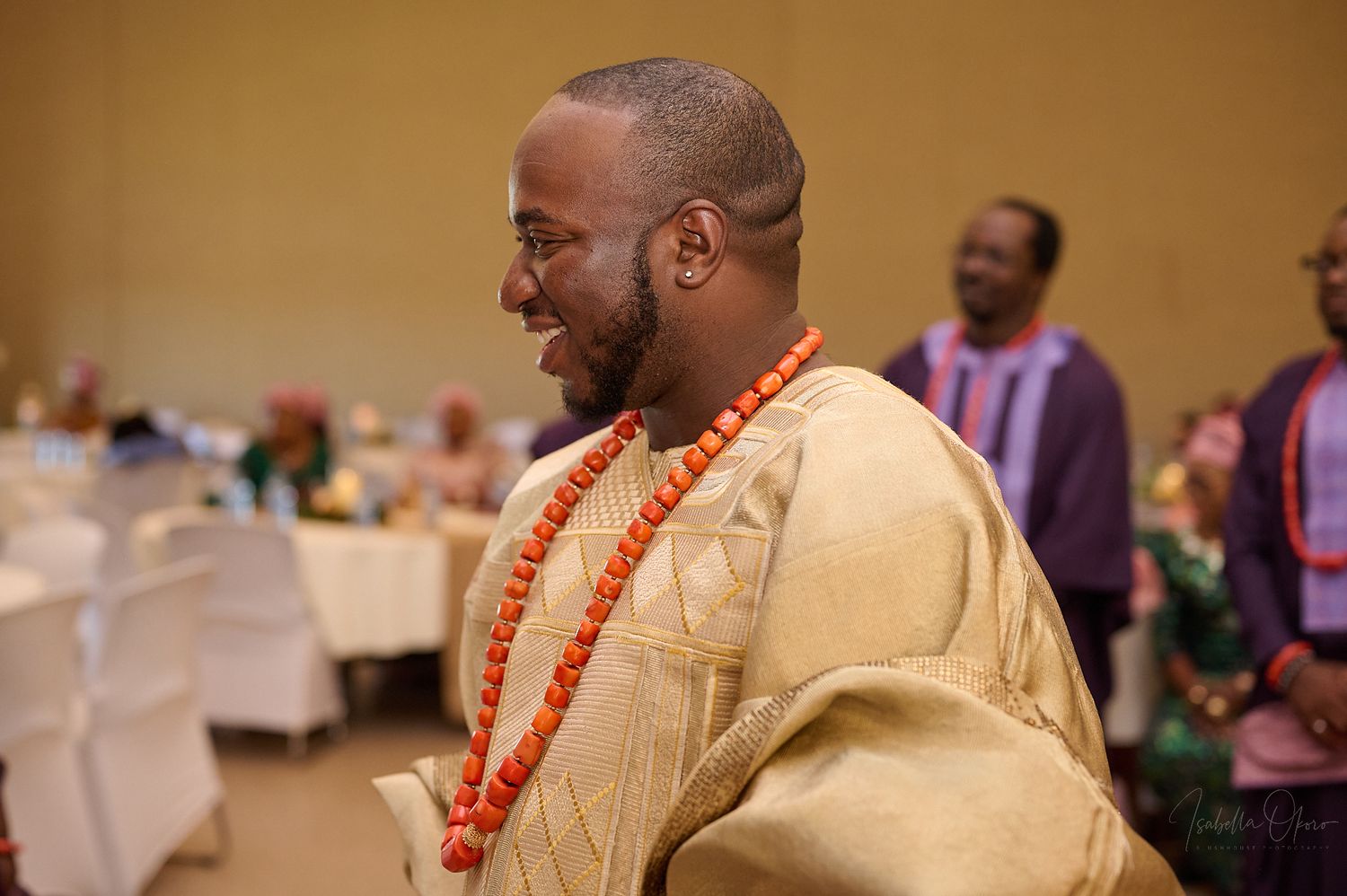 A wedding guest wearing traditional Nigerian attire and coral beads smiles during a celebration.