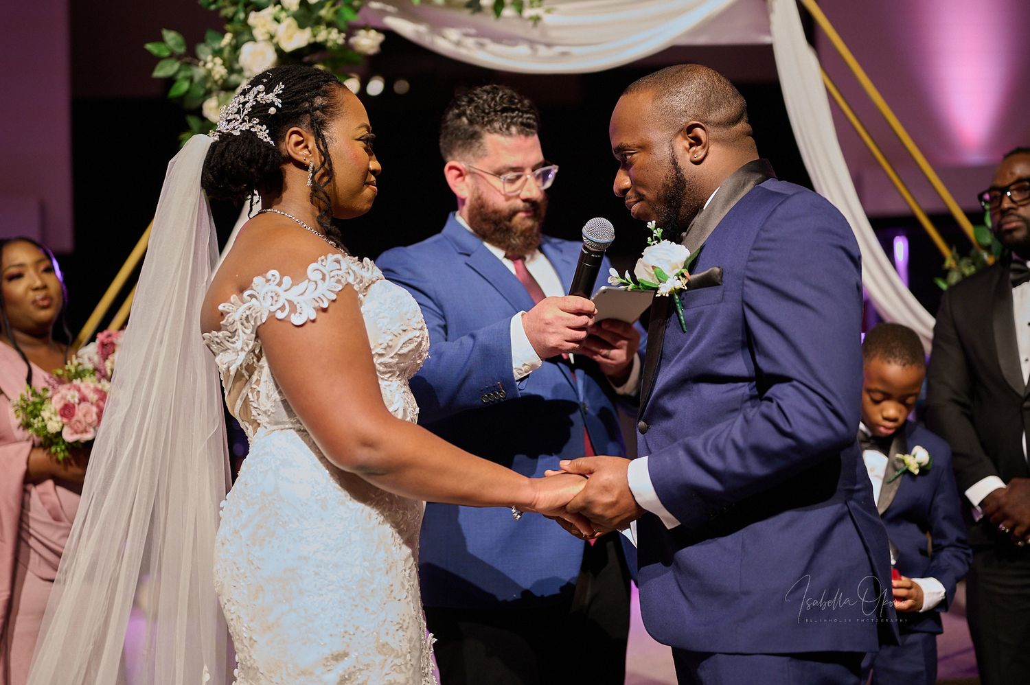 Intimate wedding ceremony moment with officiant and couple exchanging vows under floral arch.